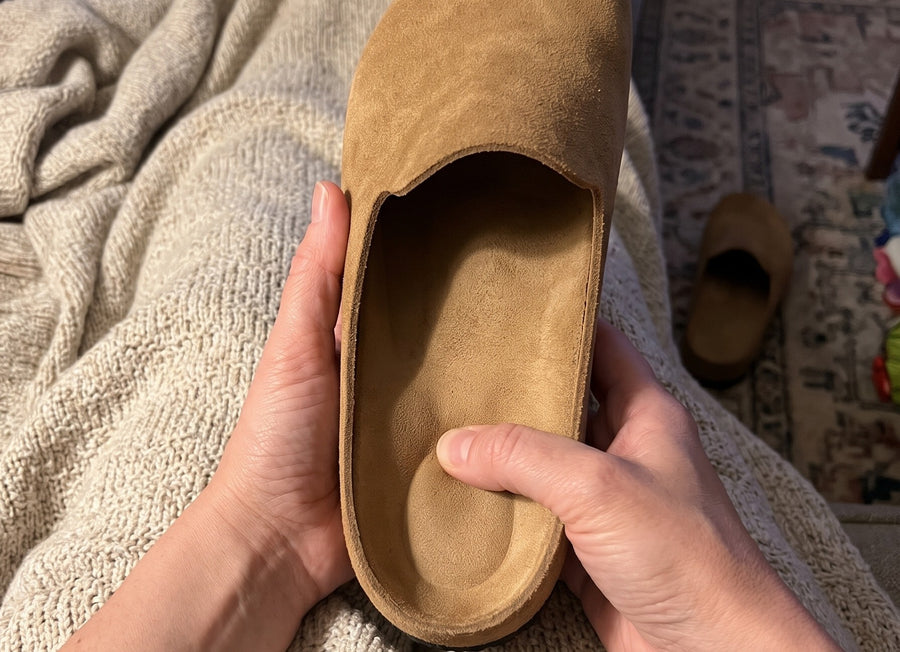 A thumb pressing into the cushioned footbed of a tan Suede Relief Clog